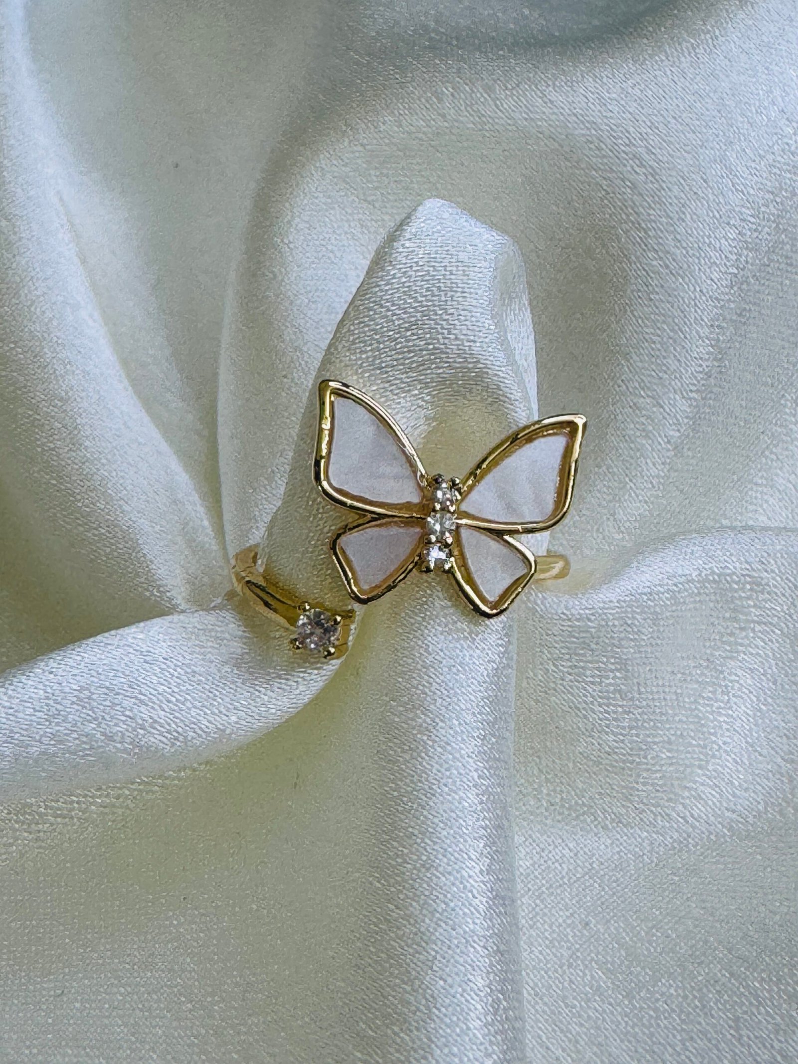Adjustable open butterfly ring with gold plating, white enamel or mother-of-pearl wings, and cubic zirconia accents.