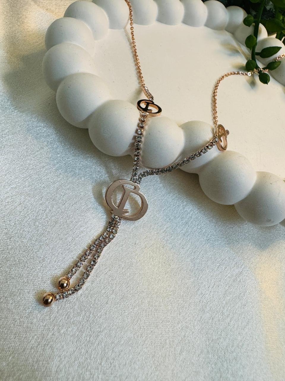 rose gold-plated, cubic zirconia-encrusted lariat-style pendant necklace featuring a prominent "D" motif.
