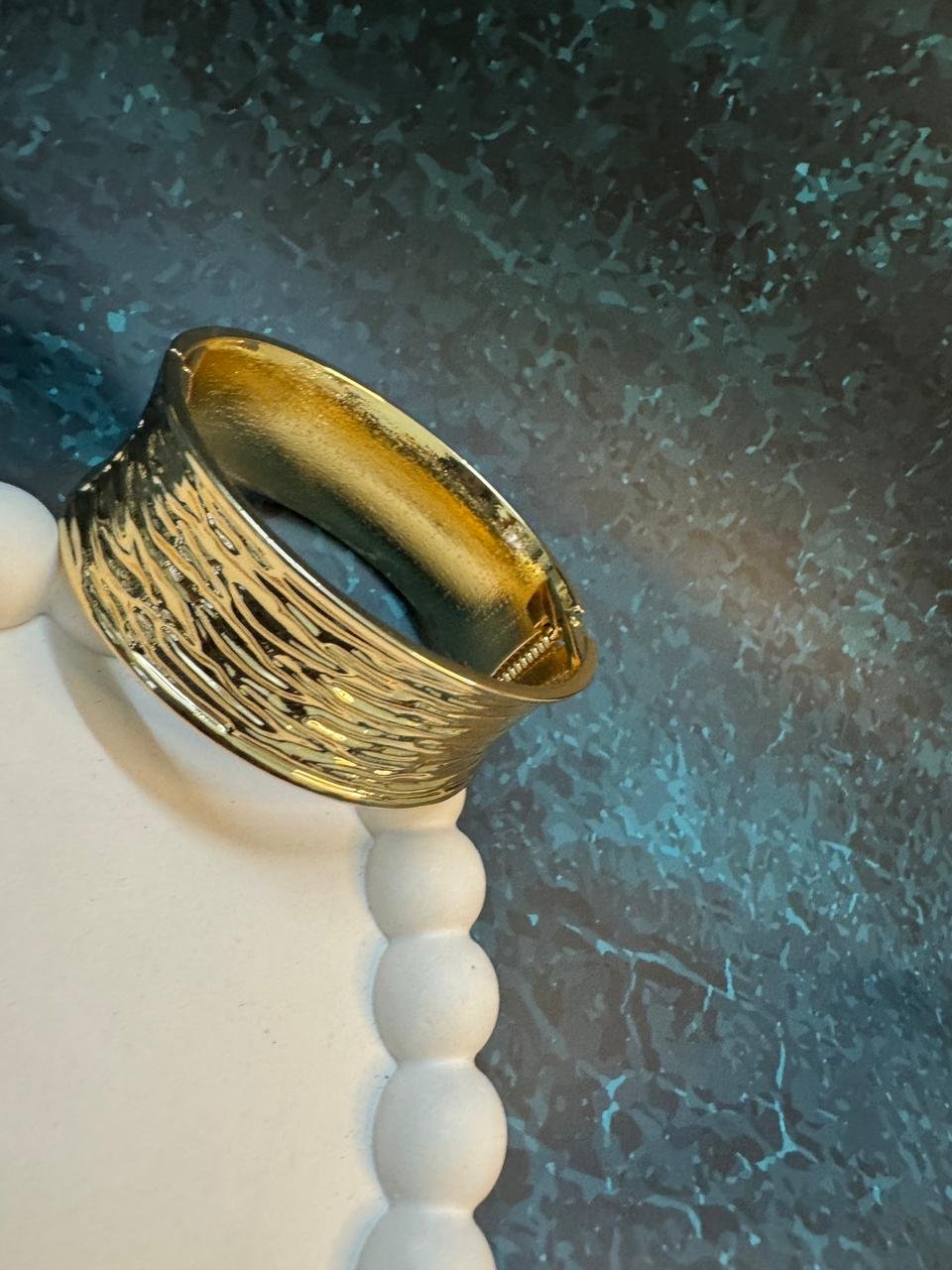 Wide gold cuff bangle with a mixed finish, combining a highly textured or wavy surface on one side with a smoother, stained finish on the other.