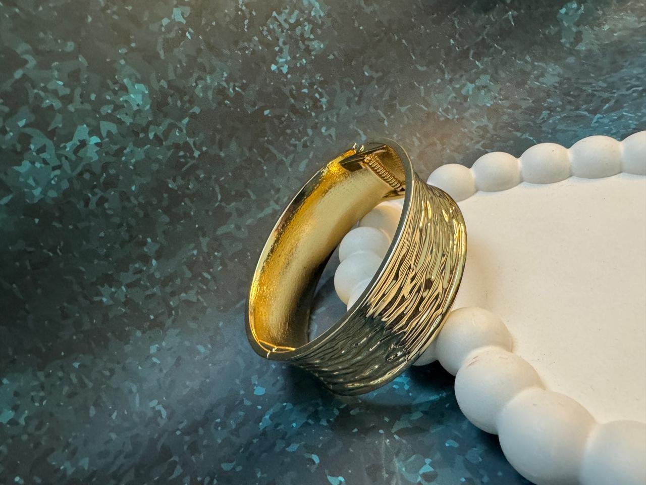 Wide gold cuff bangle with a mixed finish, combining a highly textured or wavy surface on one side with a smoother, stained finish on the other. - Image 4