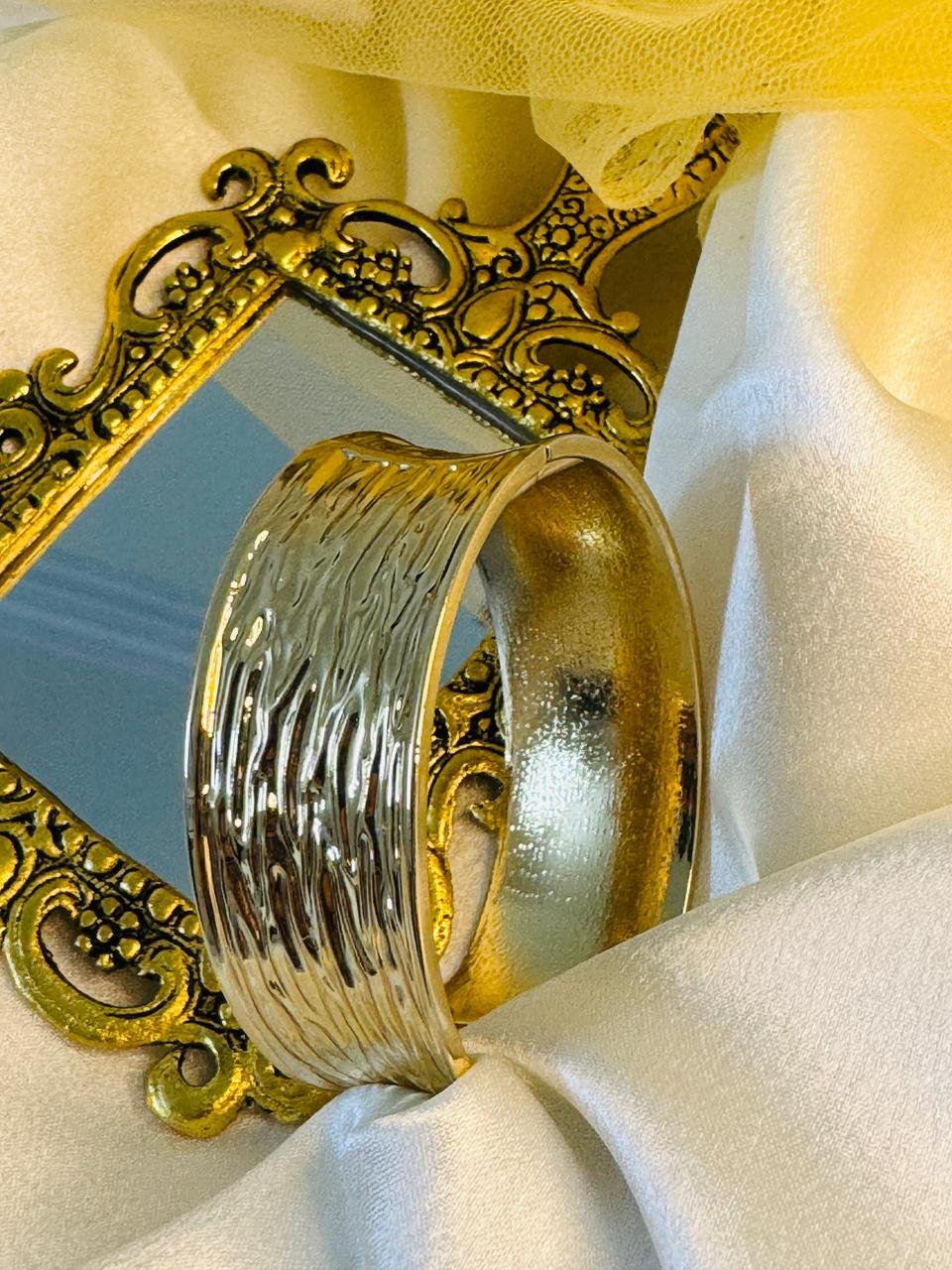 Wide gold cuff bangle with a mixed finish, combining a highly textured or wavy surface on one side with a smoother, stained finish on the other. - Image 3