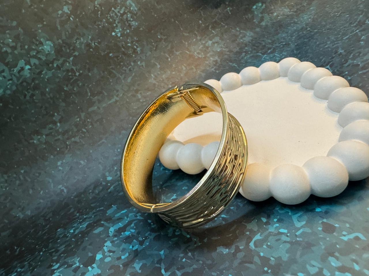 Wide gold cuff bangle with a mixed finish, combining a highly textured or wavy surface on one side with a smoother, stained finish on the other. - Image 2