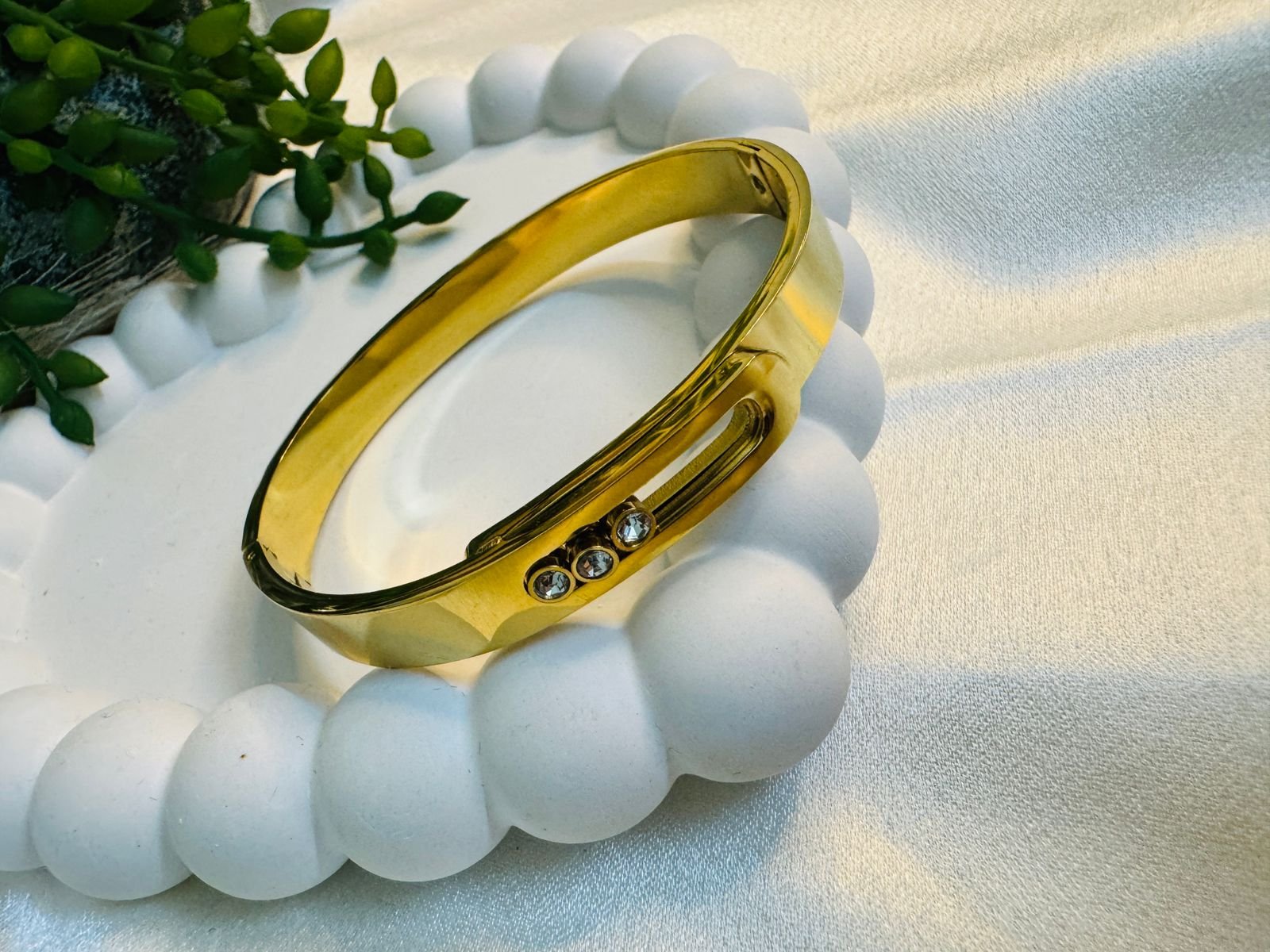 18 k gold-plated stainless steel bangle bracelet with three floating cubic zirconia stones, Anti-tarnish finish.